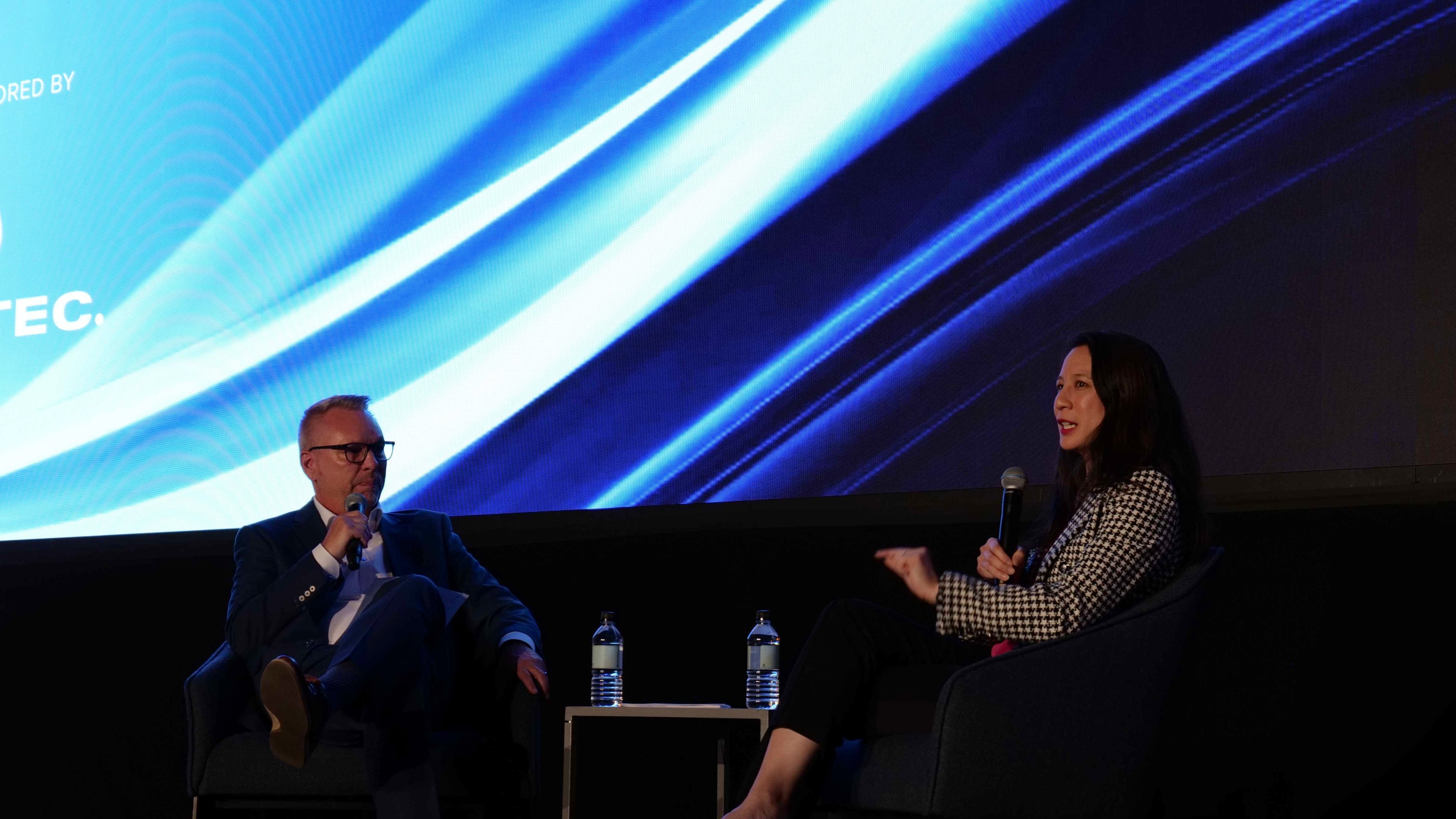 An auto auctions executive answers an interviewer's questions onstage at an industry conference. Both are seated.