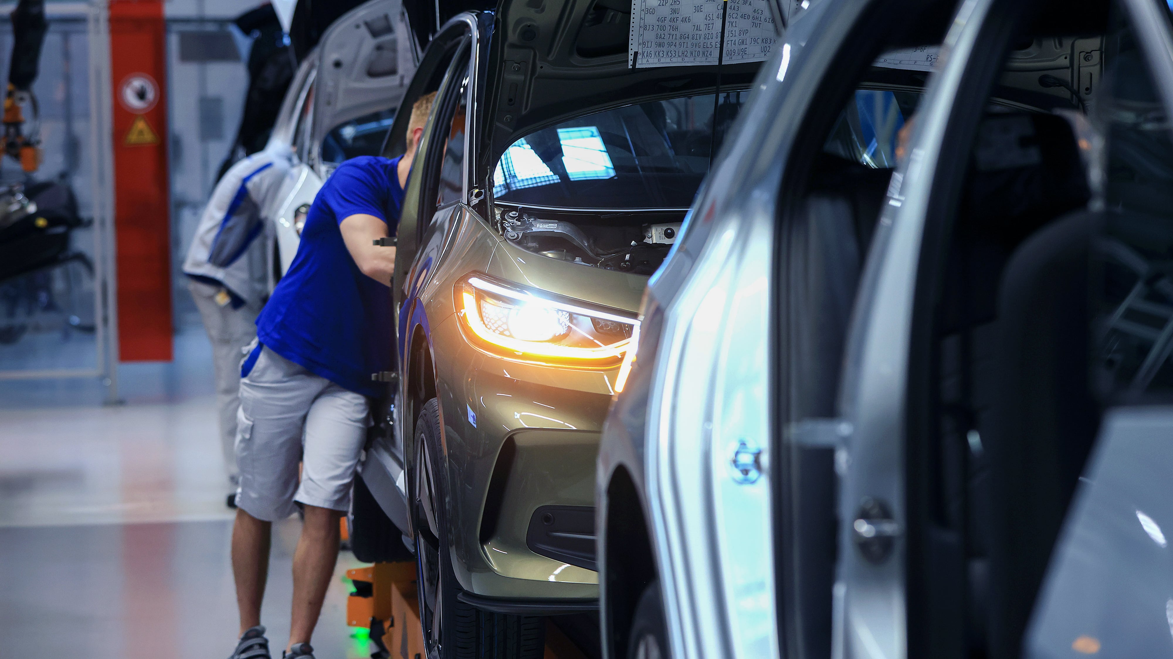 A worker stands next to a vehicle on the assembly line, with head inside the car.